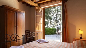 A bedroom with a checkered bedspread, a wooden wardrobe, a metal bed frame, and a view of an outdoor patio with a table and chairs. - Casale Aronne (Massa Marittima)