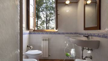 Ein Badezimmer mit Toilette, Bidet, Waschbecken und einem Fenster mit Blick auf Bäume.