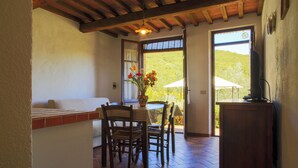 A dining area with a table, chairs, and a vase of flowers. There is a wooden cabinet and a window with a view of greenery. - Casale Aronne (Massa Marittima)