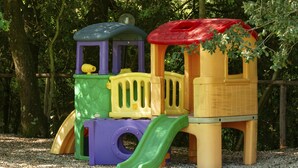 A children's play structure with a slide and climbing elements, set on a gravel surface with trees in the background. - Casale Aronne (Massa Marittima)