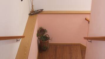 Una escalera de madera con un muro rosa, un cuadro enmarcado y una cesta de mimbre con plantas.