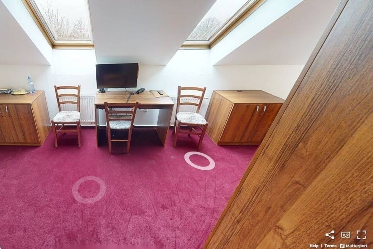 A compact room with a wooden desk, two chairs, a bed, and a TV.