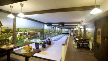 A bowling alley with wooden tables and chairs, a bowling lane, and a mural of cows on the wall.
