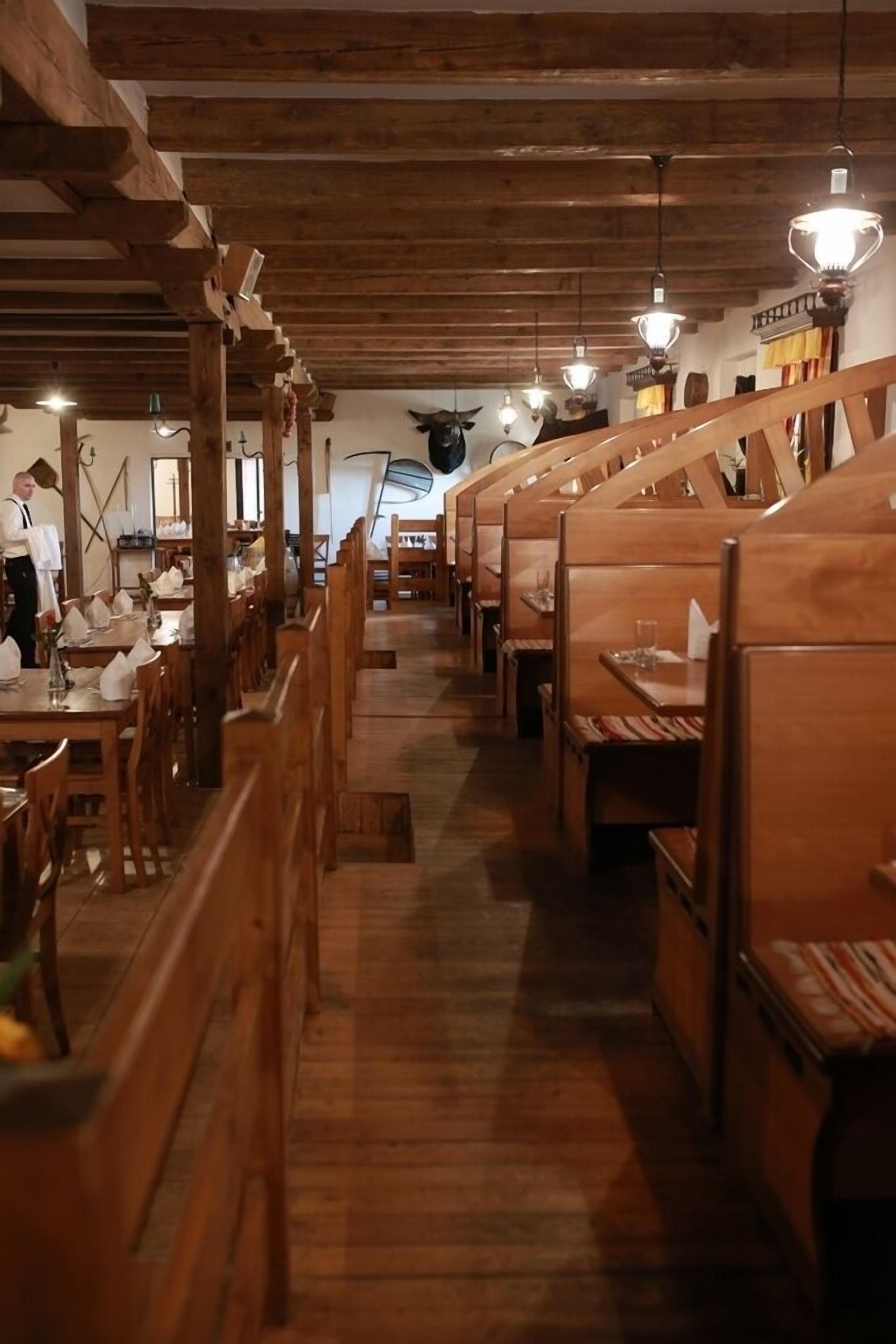 A restaurant with wooden booths and tables, a high ceiling with exposed beams, and hanging light fixtures.