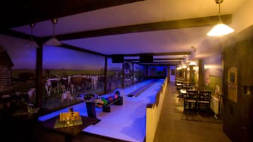 A bowling alley with a mural of cows on the wall, wooden tables, and benches.