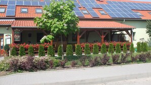 Un edificio con paneles solares en el techo, un área de estar techada con flores y un cartel.