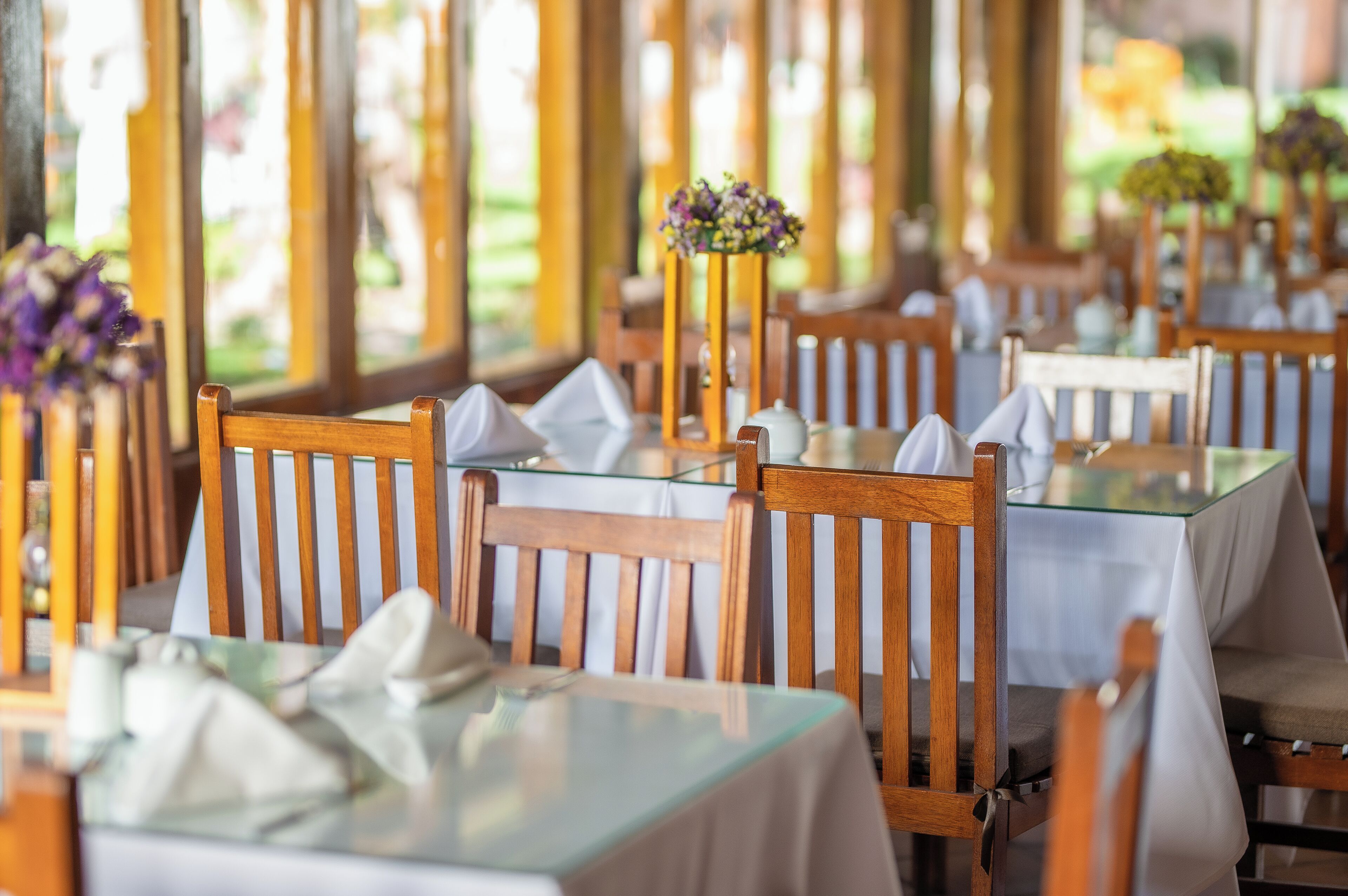 Interior de restaurante con sillas y mesas de madera, algunas con manteles blancos.