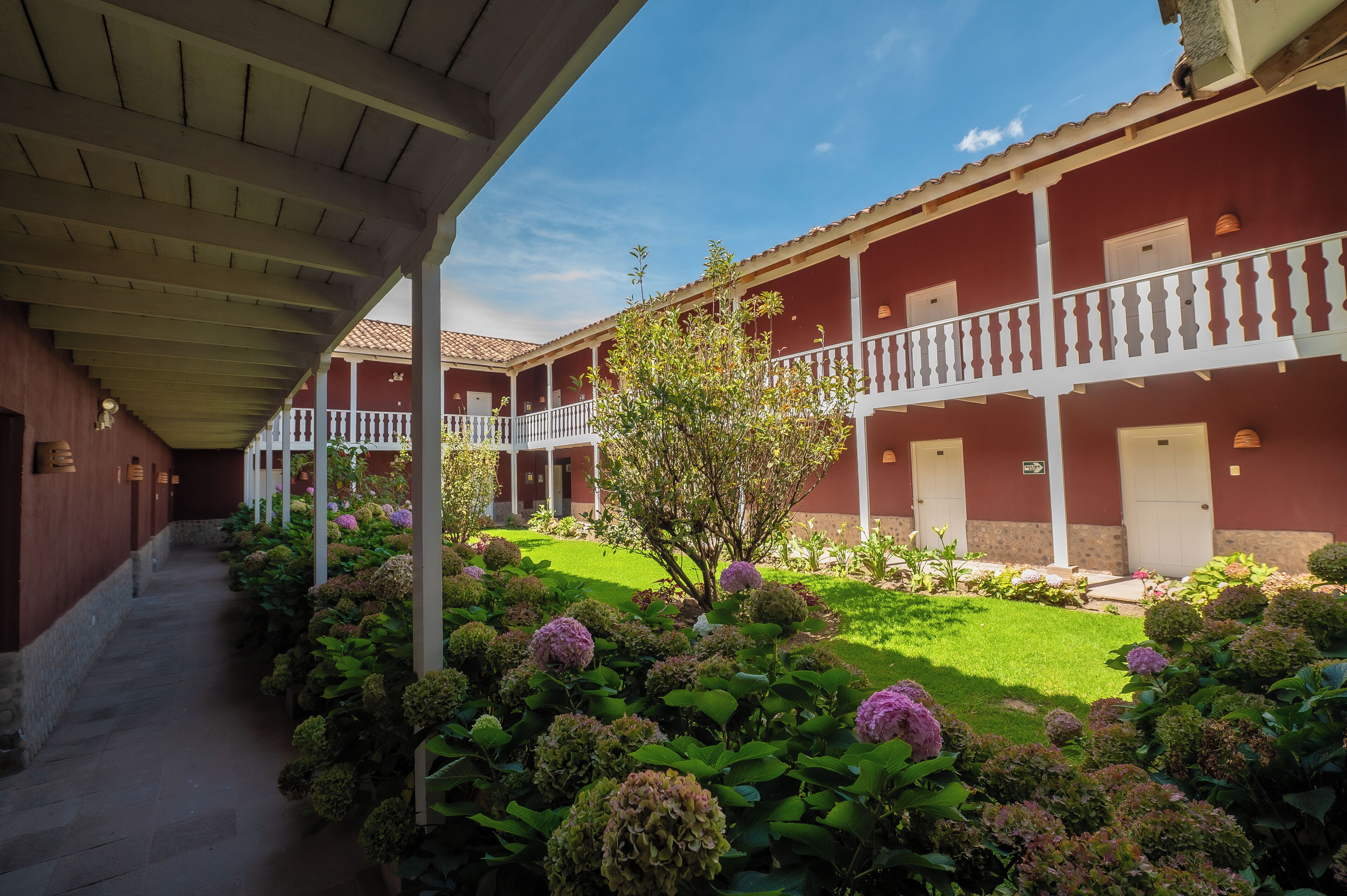 A covered walkway with a garden area featuring hydrangea plants and a clear blue sky.