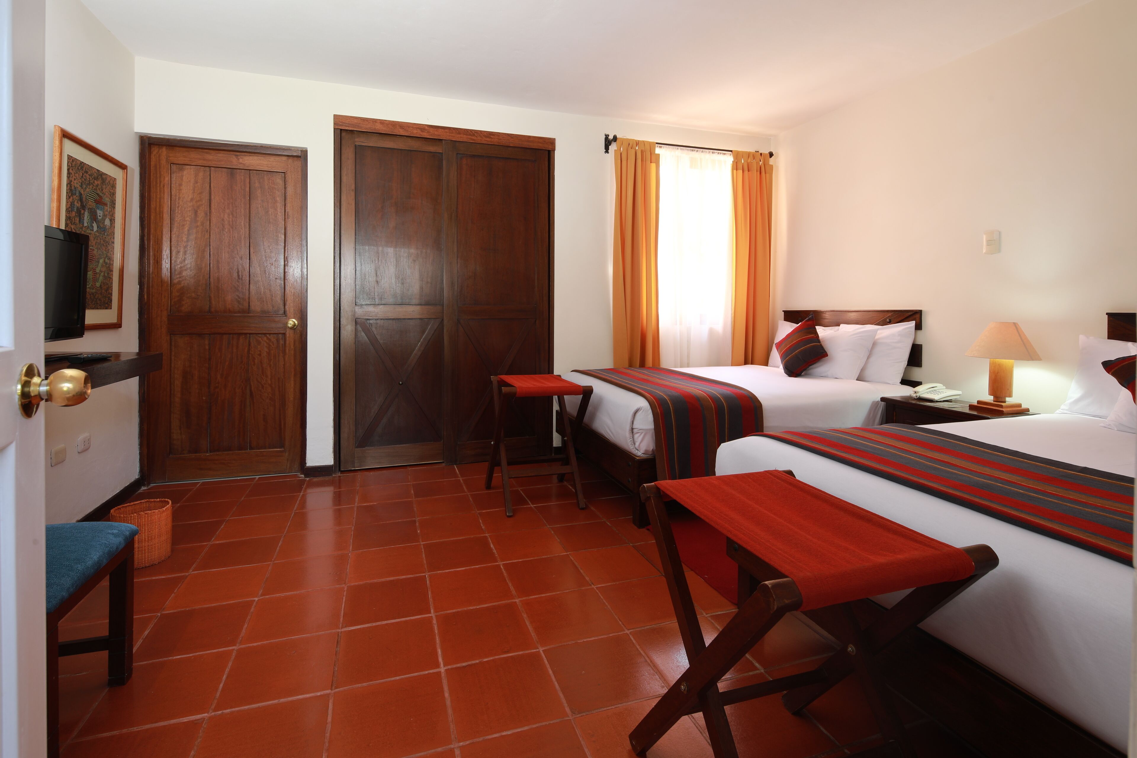 A hotel room with two beds, a desk, a chair, a television, and a door.