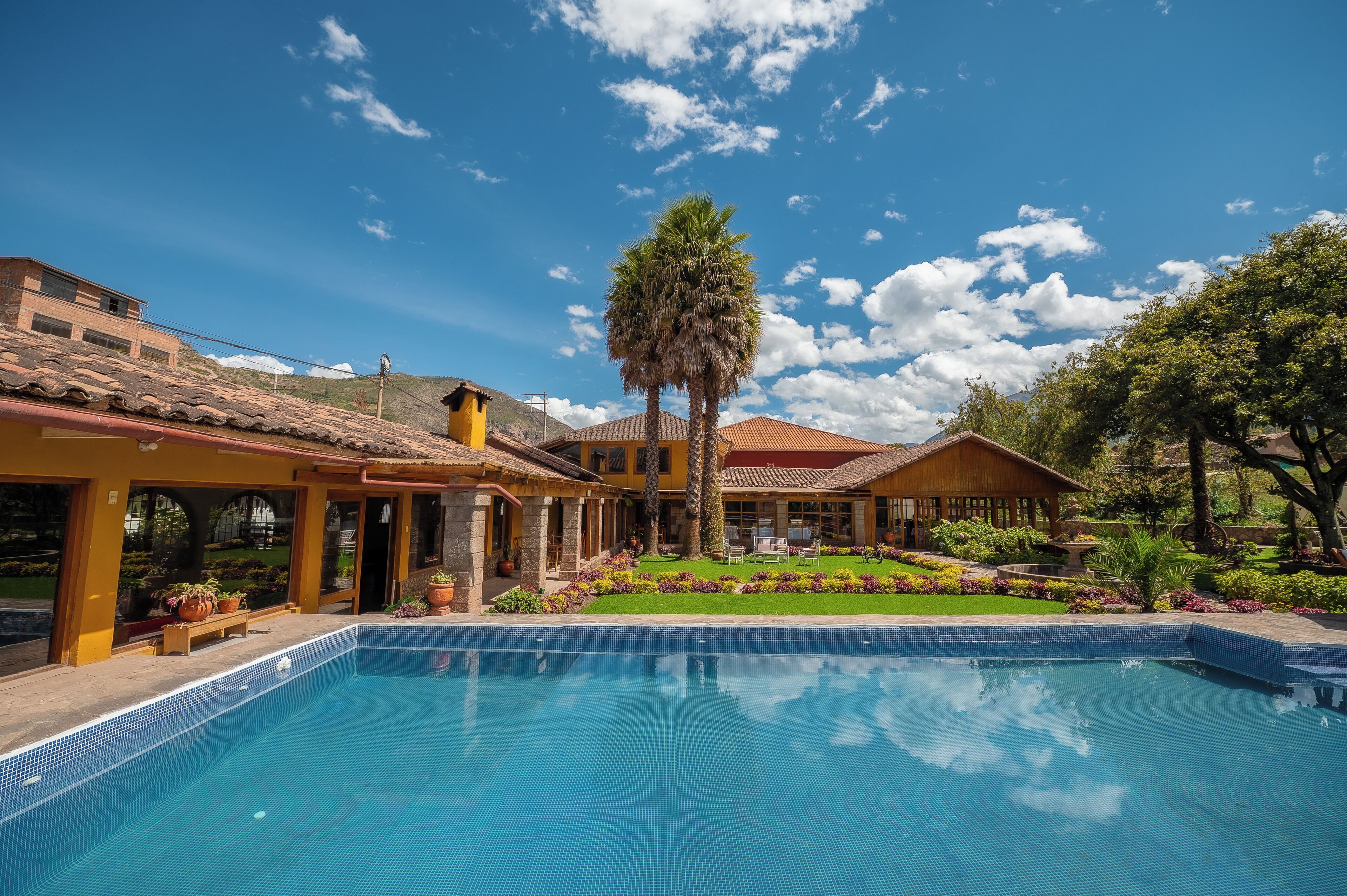 A pool area with a clear blue sky, a palm tree, and a building with a tiled roof.