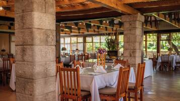 Un restaurant doté de piliers en pierre, de tables et de chaises en bois, et offrant une vue sur l’extérieur grâce à de grandes fenêtres.