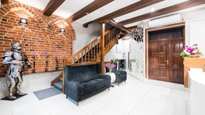 A spacious living area with a brick wall, a wooden staircase, a dark sofa, and a wooden door.