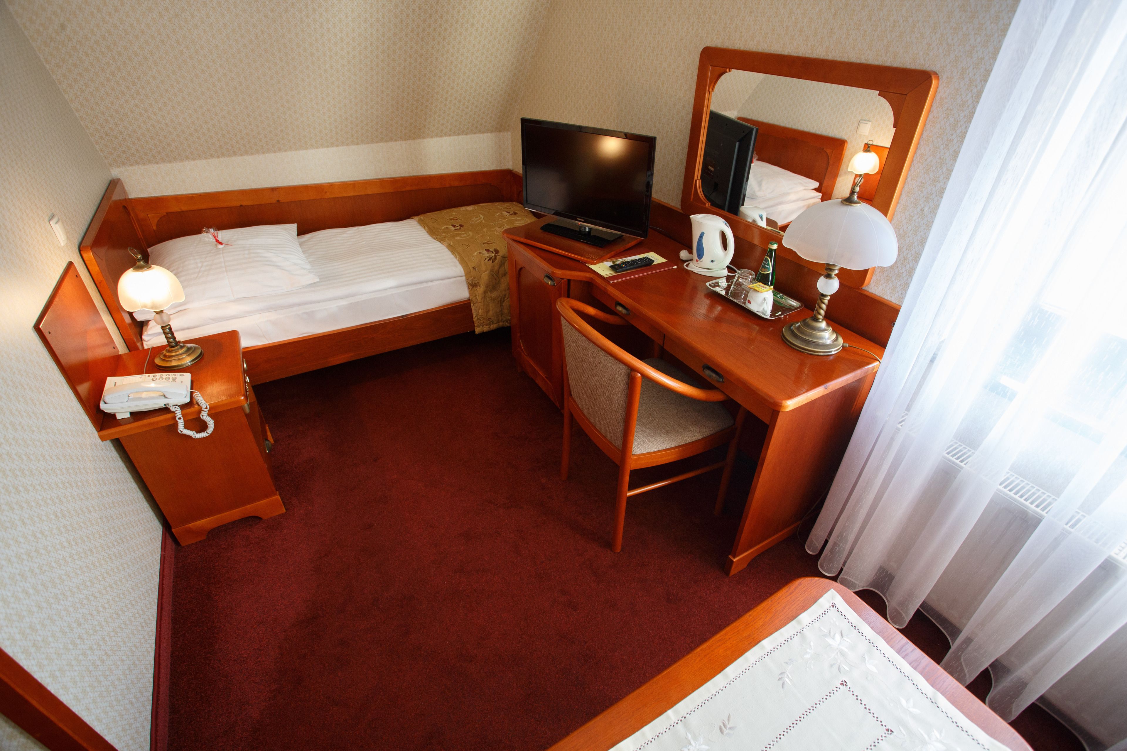 Habitación de hotel con una cama individual, un escritorio con silla, televisión, teléfono y espejo.