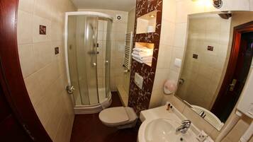 Ein Badezimmer mit einer Duschkabine, einer Toilette, einem Waschbecken inklusive Spiegel und einem Handtuchhalter.