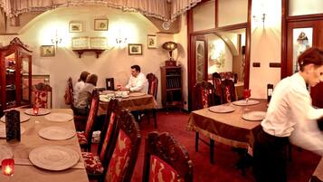 A formal dining room with a long table set for a meal, surrounded by ornate chairs.