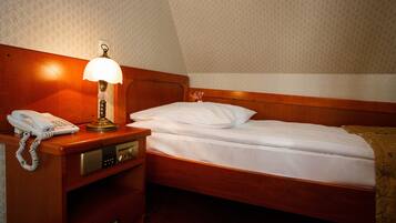 Een hotelkamer met een houten hoofdeinde, een bed met witte lakens, een bedlampje, een telefoon en een klein nachtkastje.