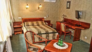 A room with a bed, a wooden desk, a chair, a small table, and two wall-mounted lamps.