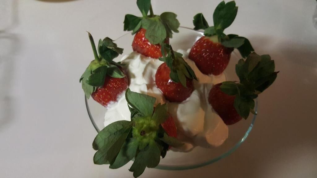A bowl of strawberries with whipped cream and leaves.