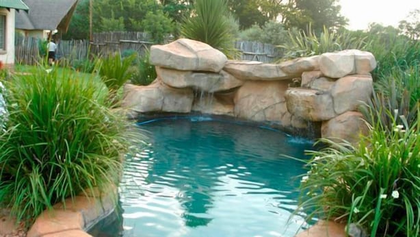Un jardin à l’arrière de la maison, doté d’une piscine entourée d’une cascade artificielle en roches et d’une végétation luxuriante.