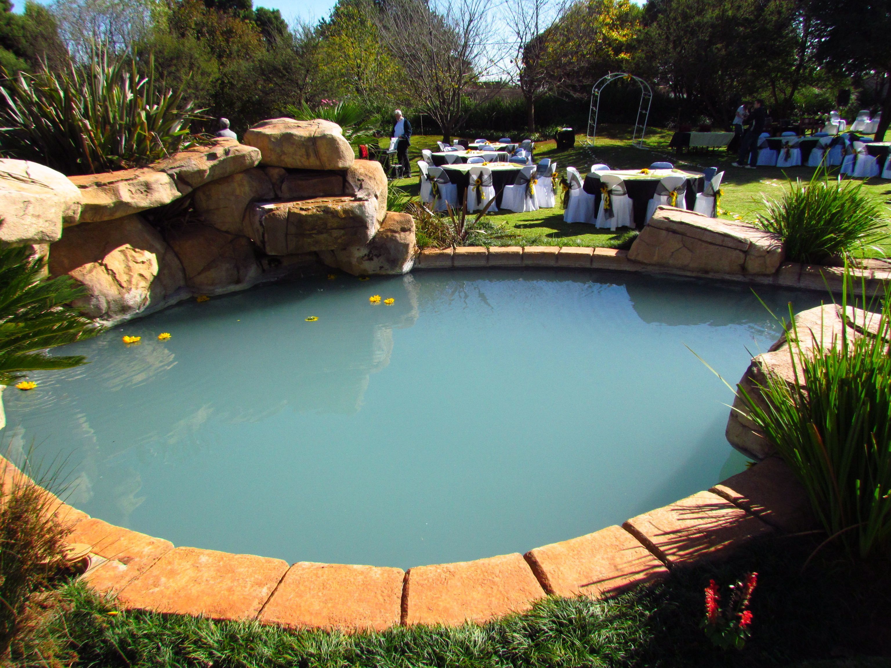Una piscina circular con borde de roca natural, rodeada de mesas y sillas para comidas al aire libre.