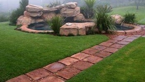 Un jardin aménagé avec un élément décoratif en roche, un chemin pavé et de la pelouse.