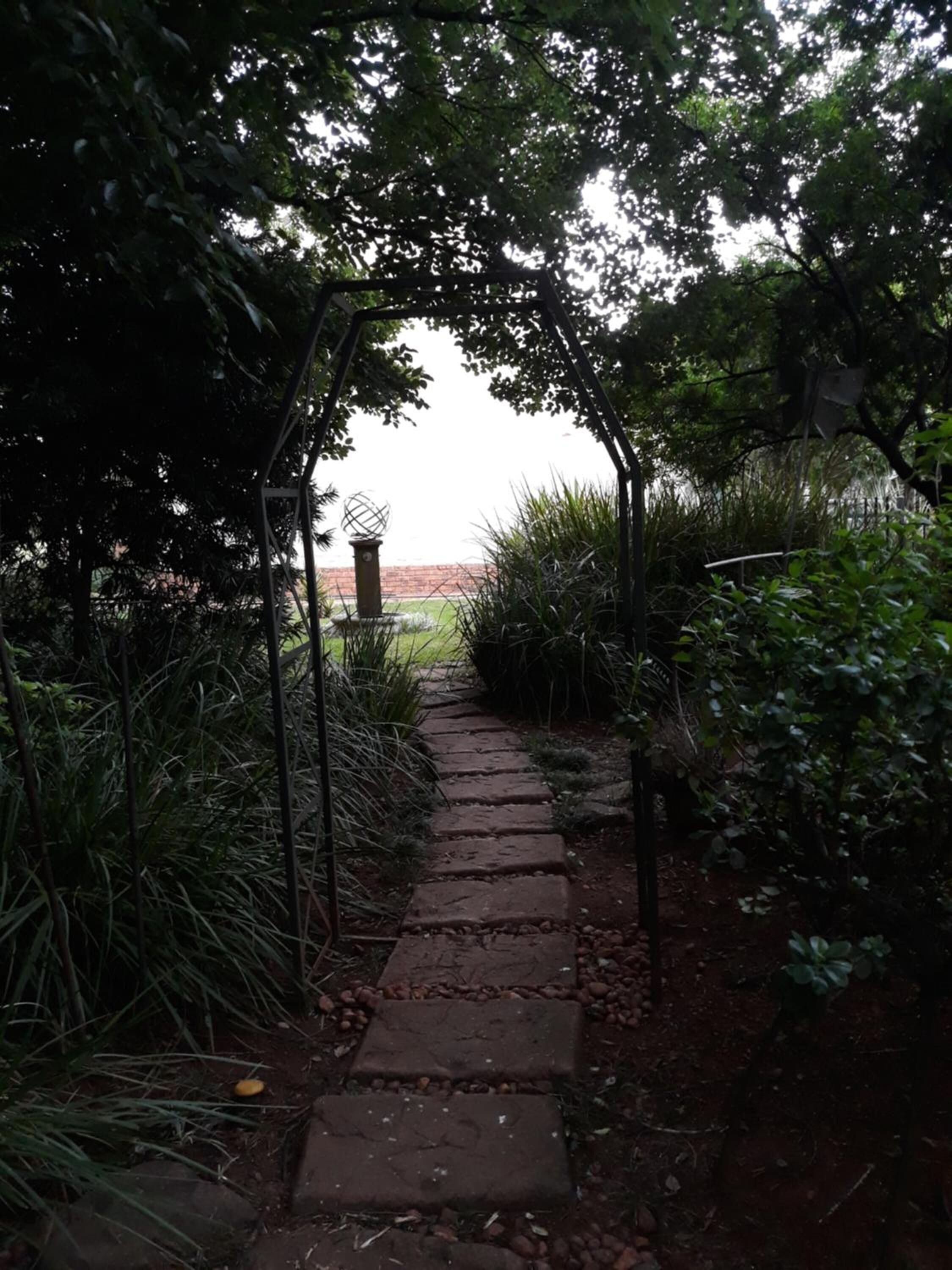 A stone pathway leading through a garden with a metal archway.