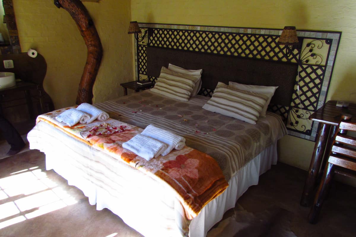 A bed with a patterned bedspread and pillows, a wooden headboard, and a nightstand with a lamp.