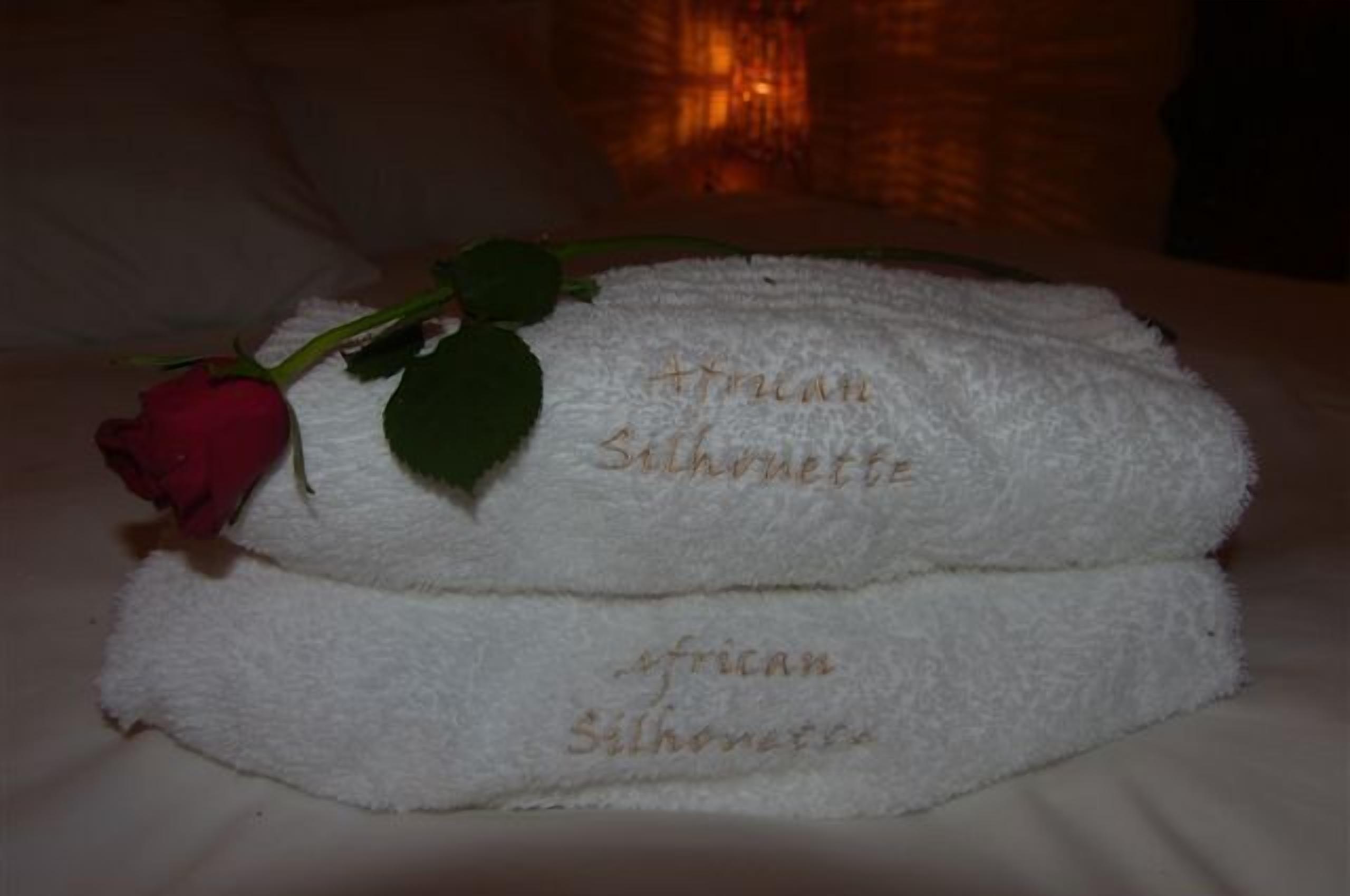 Een bed met twee witte handdoeken met de tekst 'African Silhouette' en een enkele rode roos.