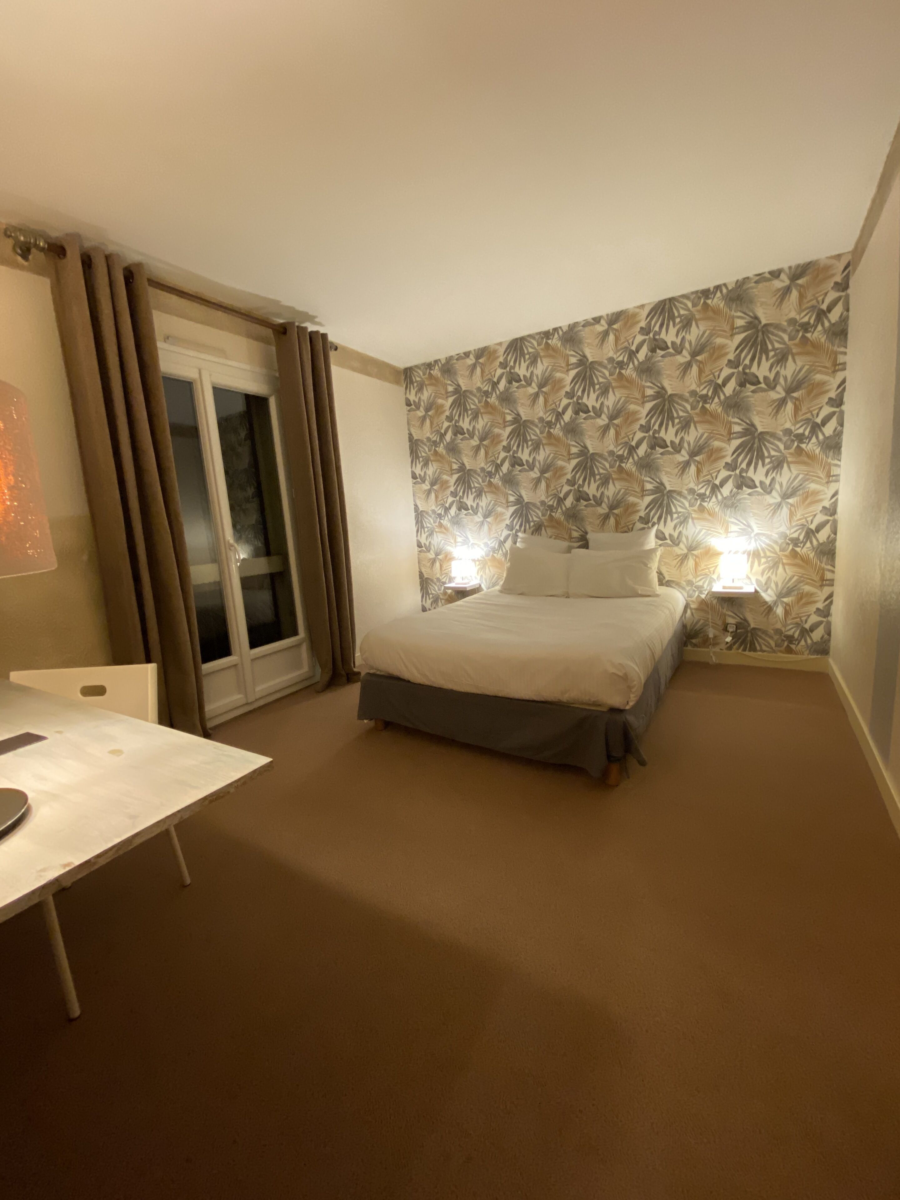 A hotel room with a bed, a desk, and a window with curtains.