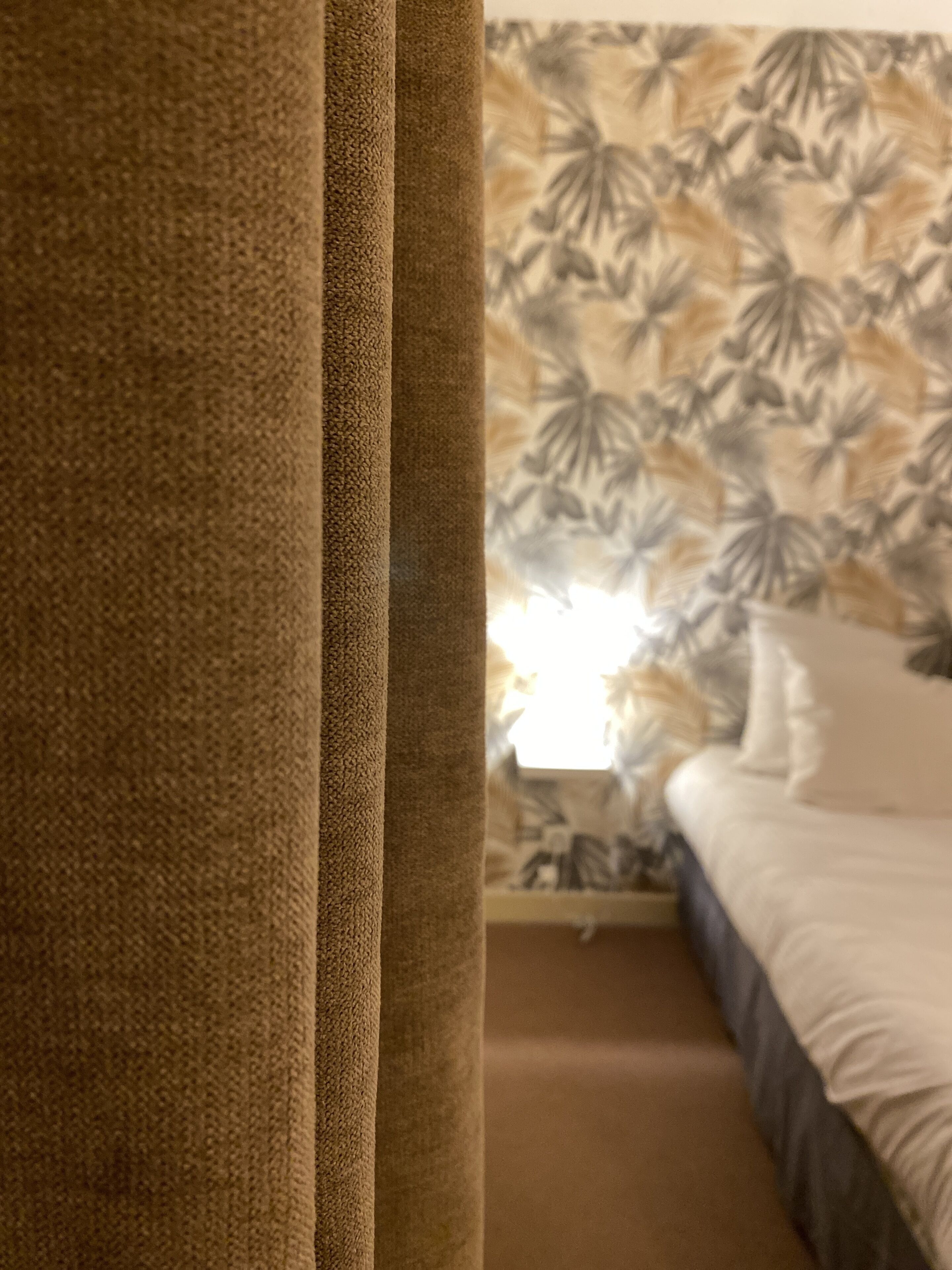 A bedroom with a bed, a nightstand, and a window with curtains.