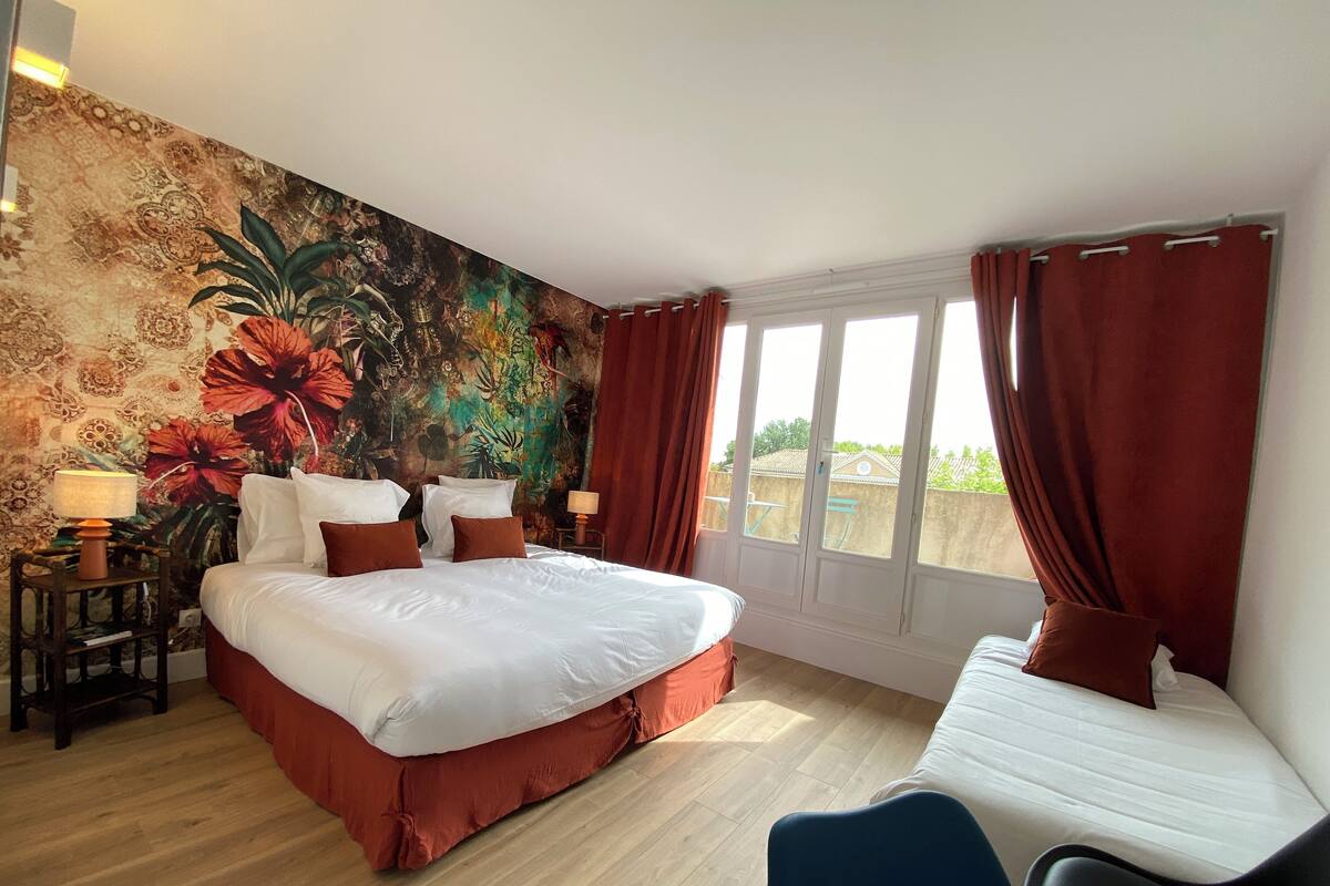 A bedroom with a large bed, a desk, and a window with curtains.