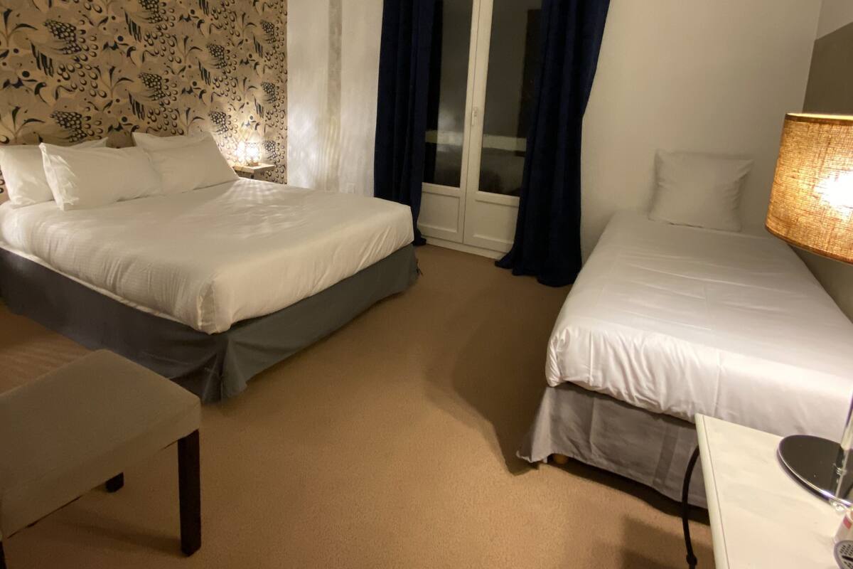 A hotel room with two beds, a desk, a chair, a lamp, and a door with curtains.