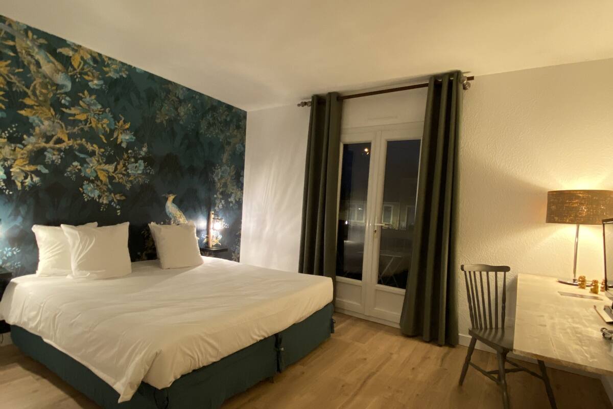 A bedroom with a bed, a chair, a table, and a window with curtains.