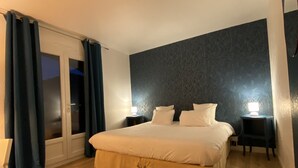 A bedroom with a large bed, dark patterned wall, wooden flooring, and a sliding glass door with curtains. - Logis Hôtel Médiéval, Montélimar Nord (Rochemaure)