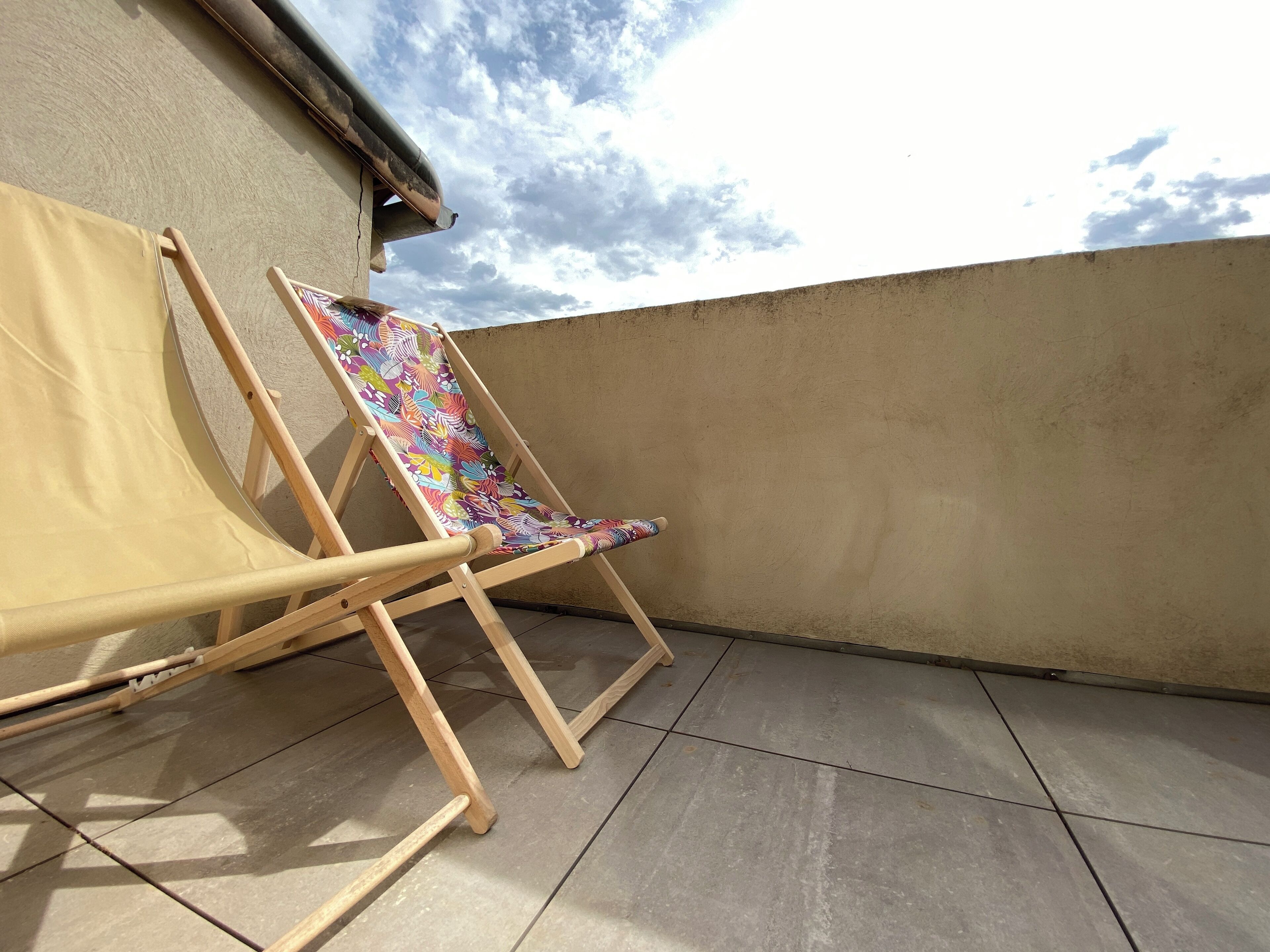 Ein bequemer Holzliegestuhl mit bunten Stoffpolstern auf einer gefliesten Balkon.