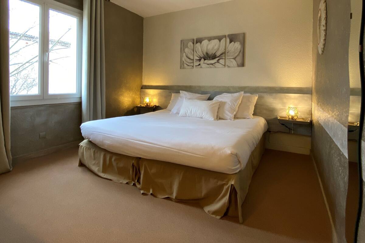 A bedroom with a large bed, a window with curtains, a wall-mounted flower painting, and bedside lamps.