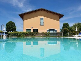 Un edificio con piscina frente a él, rodeado de vegetación y un cielo despejado.