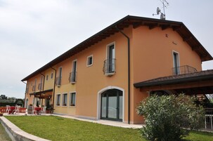 Un edificio de dos pisos con techo plano, varios balcones y un patio cubierto con mobiliario exterior.