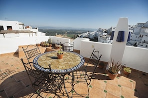 A rooftop terrace with a round table and chairs, potted plants, and a view of a coastal town. - La Casa del Califa (Vejer de la Frontera)