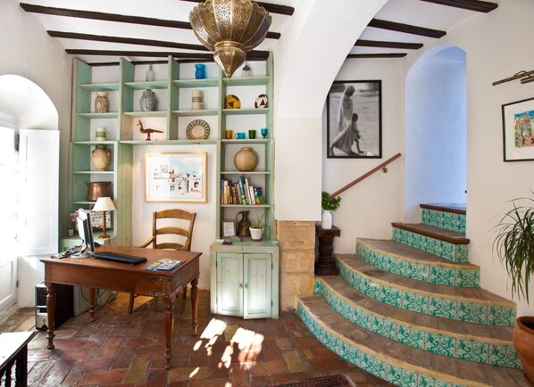 A room with a wooden desk, a bookshelf, a staircase with patterned tiles, and a hanging light fixture. - La Casa del Califa (Vejer de la Frontera)