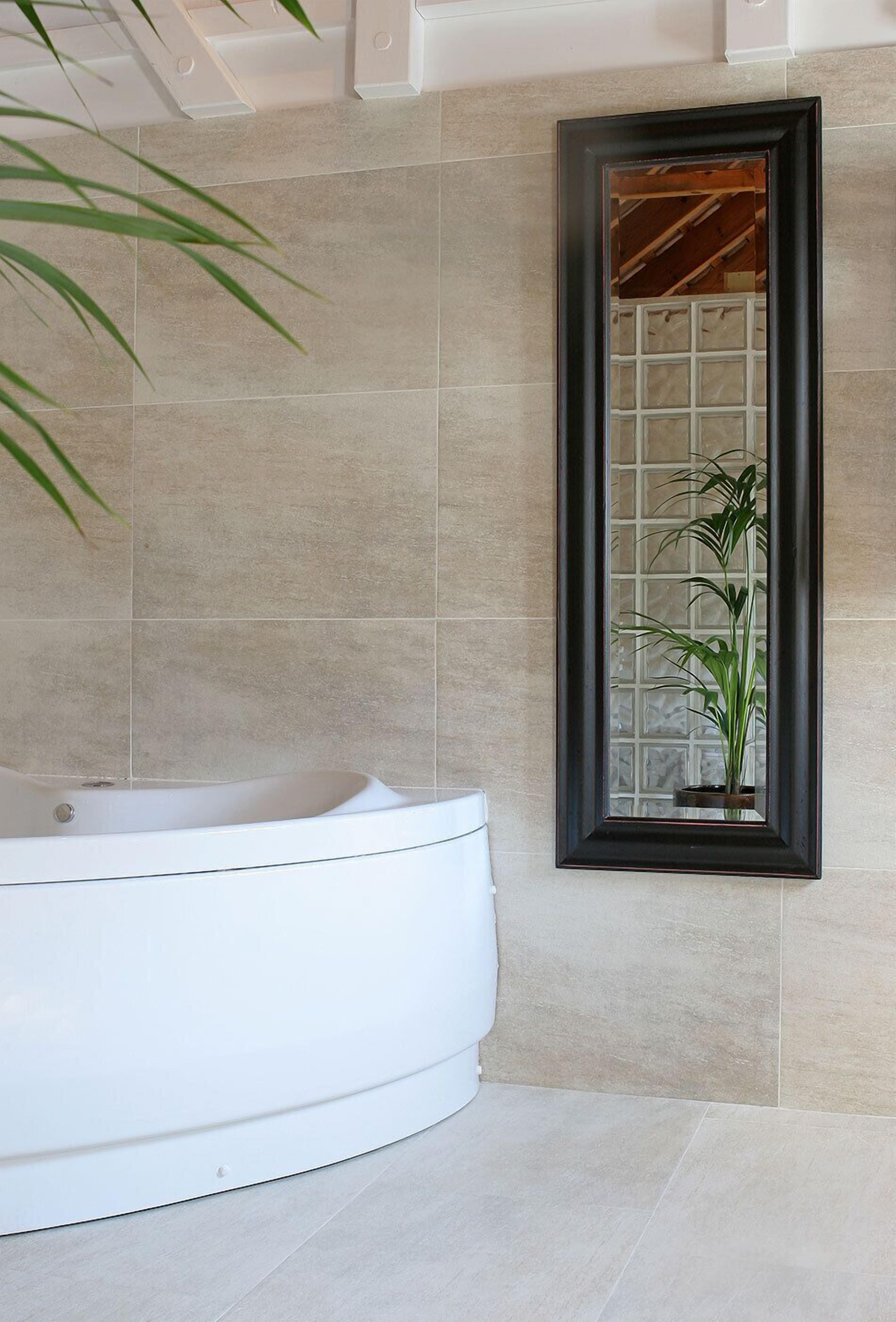 A modern bathroom with a freestanding bathtub, a large mirror, and a potted plant.
