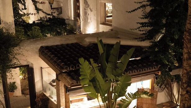 An outdoor patio with a dining area, potted plants, and a building with a tiled roof. - La Casa del Califa (Vejer de la Frontera)