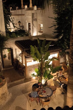 An outdoor patio with a dining area, potted plants, and a building with a tiled roof. - La Casa del Califa (Vejer de la Frontera)