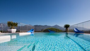 A clear blue pool with lounge chairs and potted plants, surrounded by a metal fence and mountains in the background. - Residence Verdeluna (Pietrasanta)