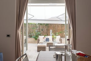 An open-plan living area with a sofa, coffee table, and dining table, connected to a balcony with plants and a wicker chair. - Residence Verdeluna (Pietrasanta)