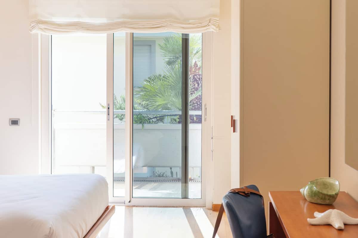 Una camera da letto con un letto, una scrivania, una sedia, una borsa e una porta vetrata scorrevole che dà su un'area esterna.