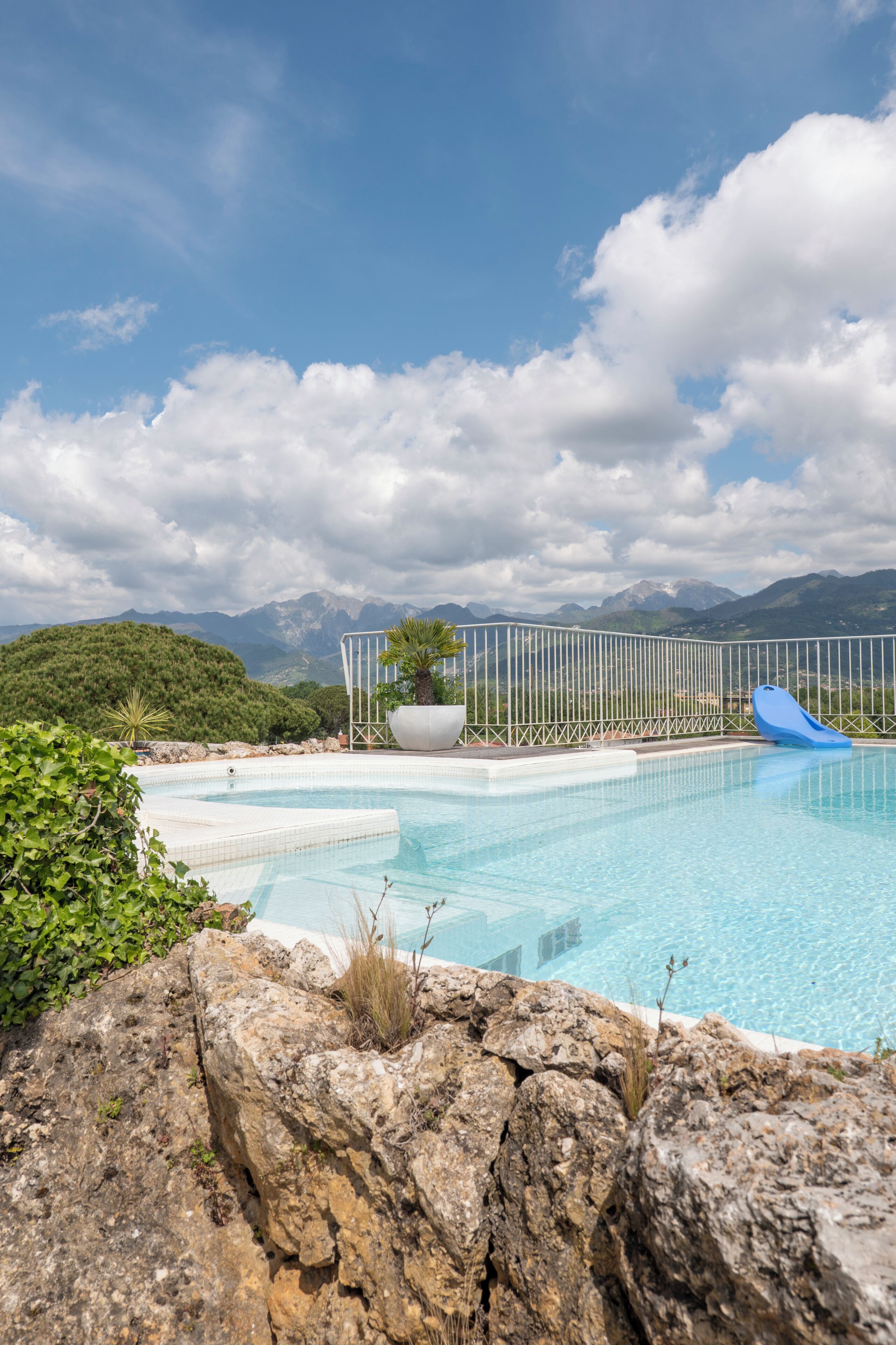 Una piscina con tobogán, rodeada por una valla, con montañas al fondo.