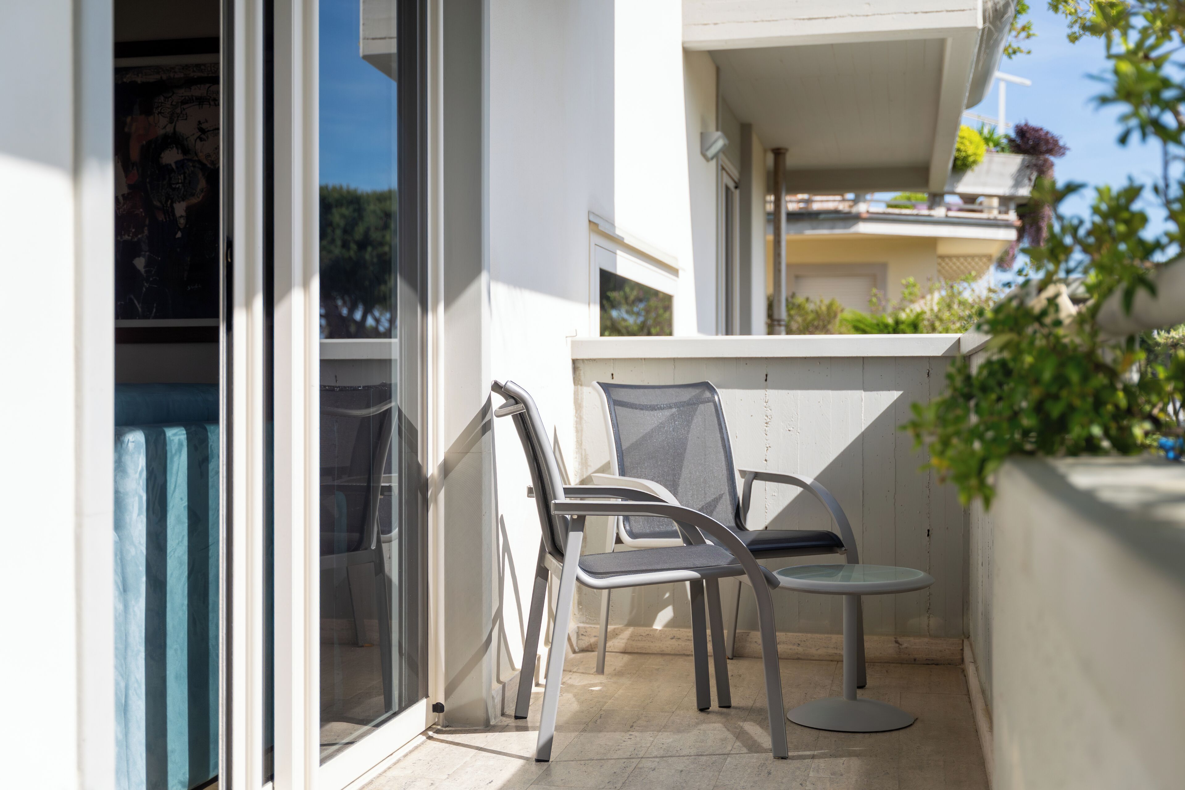 A balcony with two chairs and a table, a sliding glass door, and a view of a building with balconies.