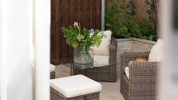 Un área de estar al aire libre con muebles de mimbre, una mesa de vidrio, cojines y un florero con flores.