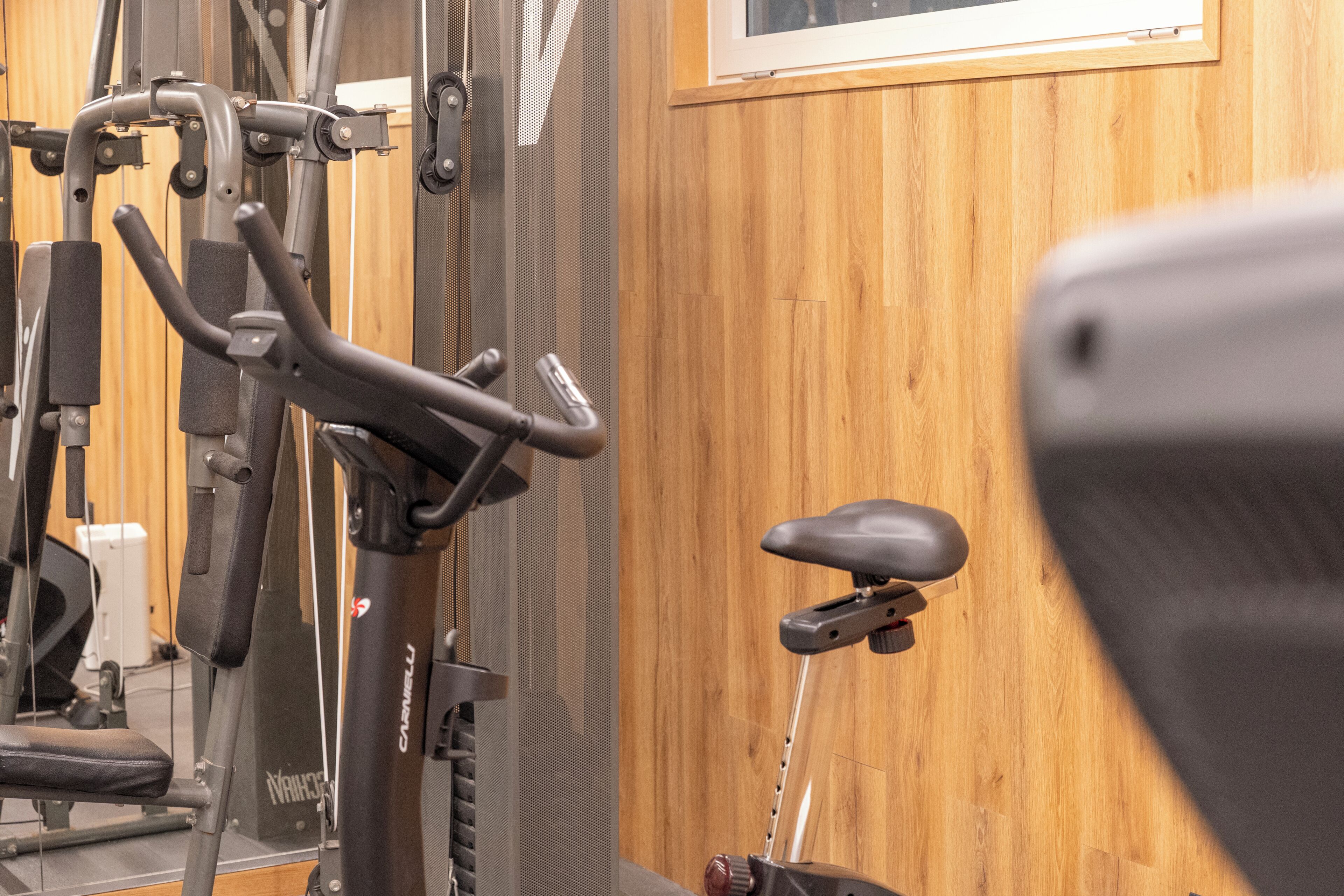 A gym with exercise equipment, a wooden wall, and a window.